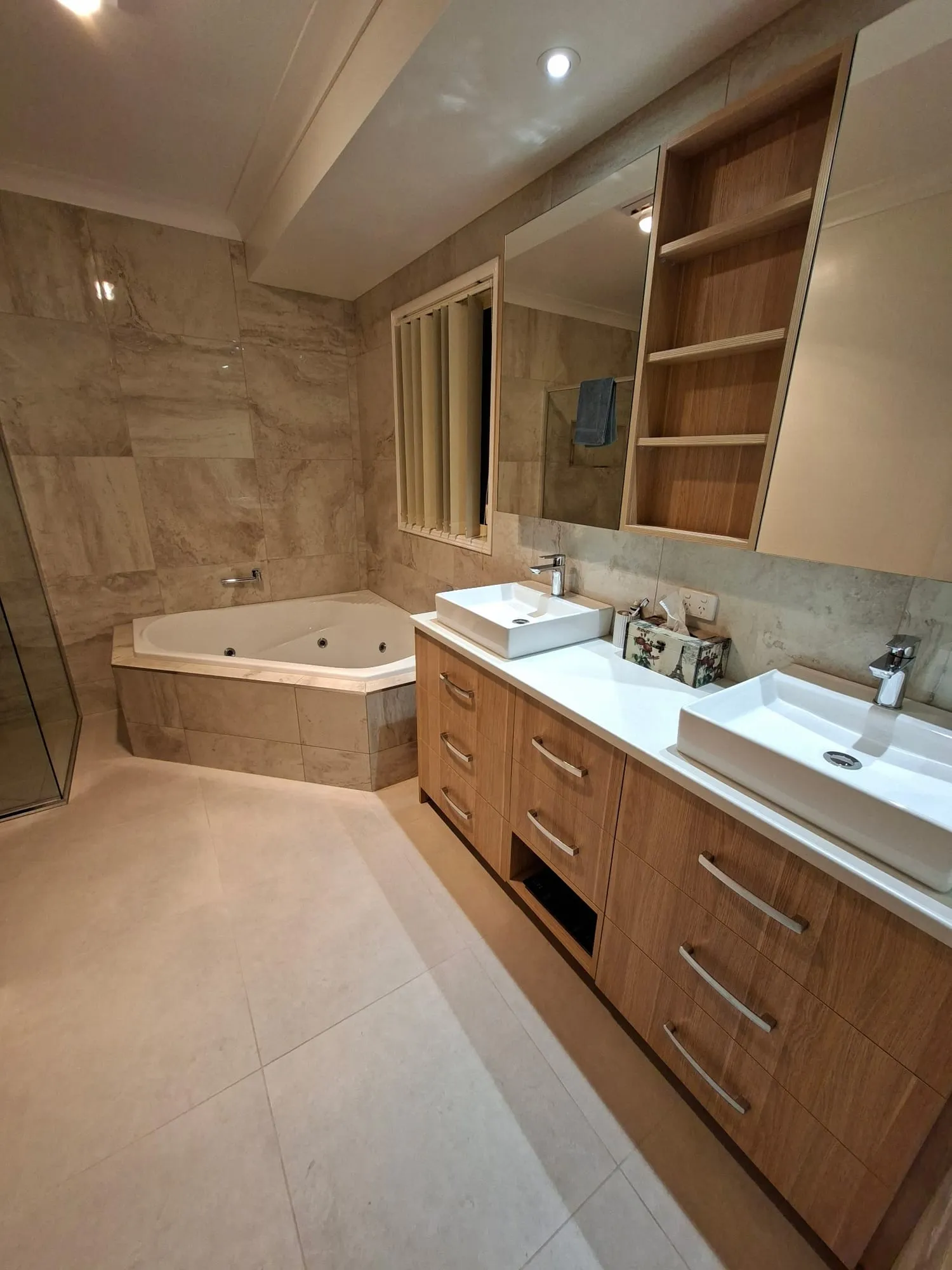 Corner spa bath and a timber double vanity with twin vessel basins, under open shelving