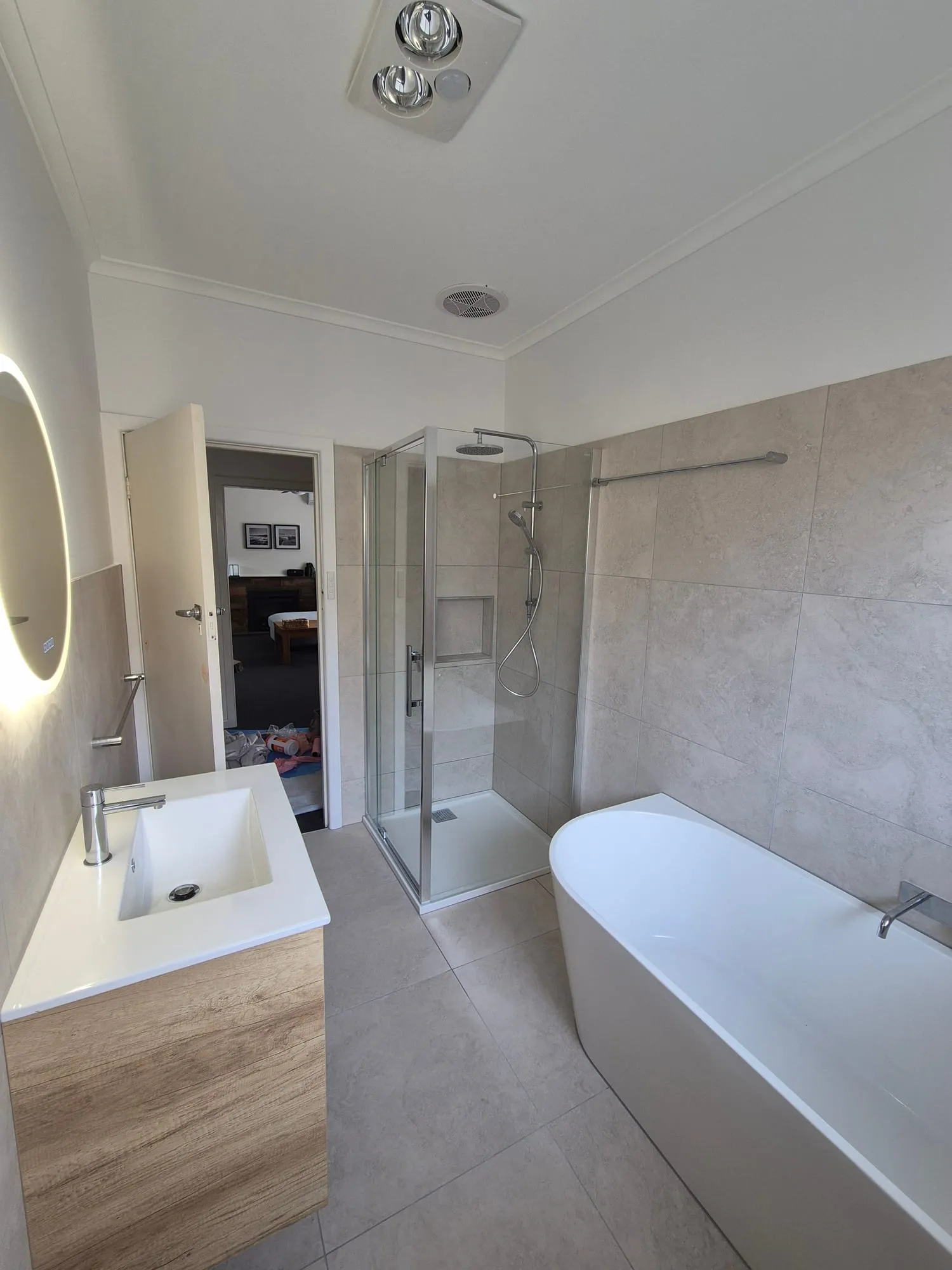 Bathroom with a timber vanity, a shower and a freestanding bath, under a backlit round mirror