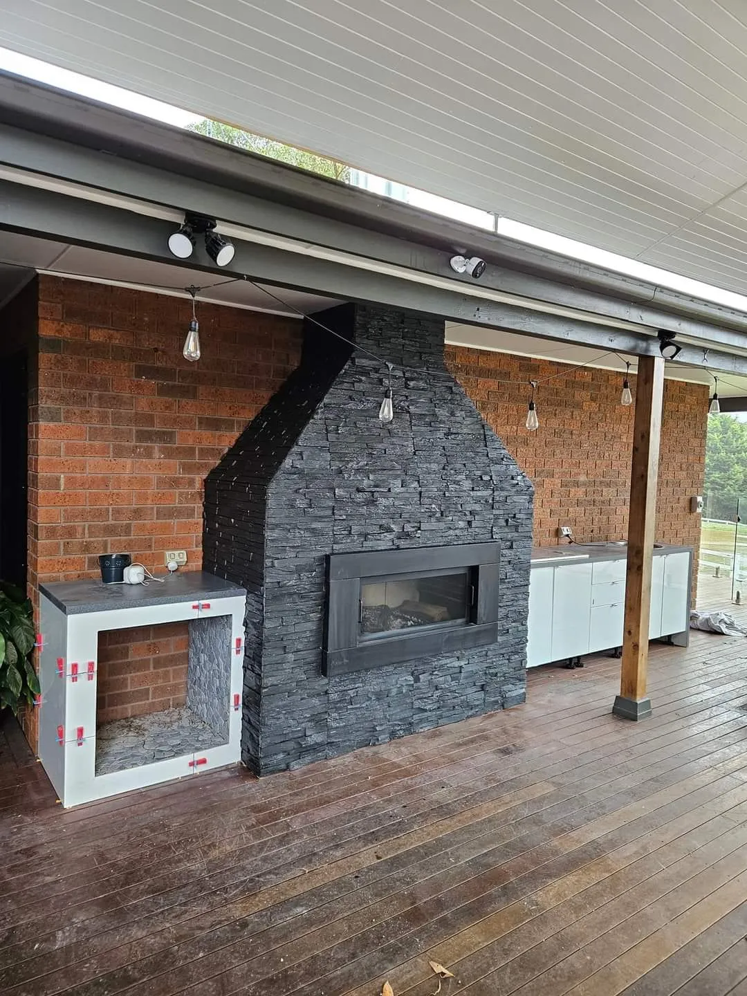 Covered outdoor area with a stacked stone fireplace and a timber deck