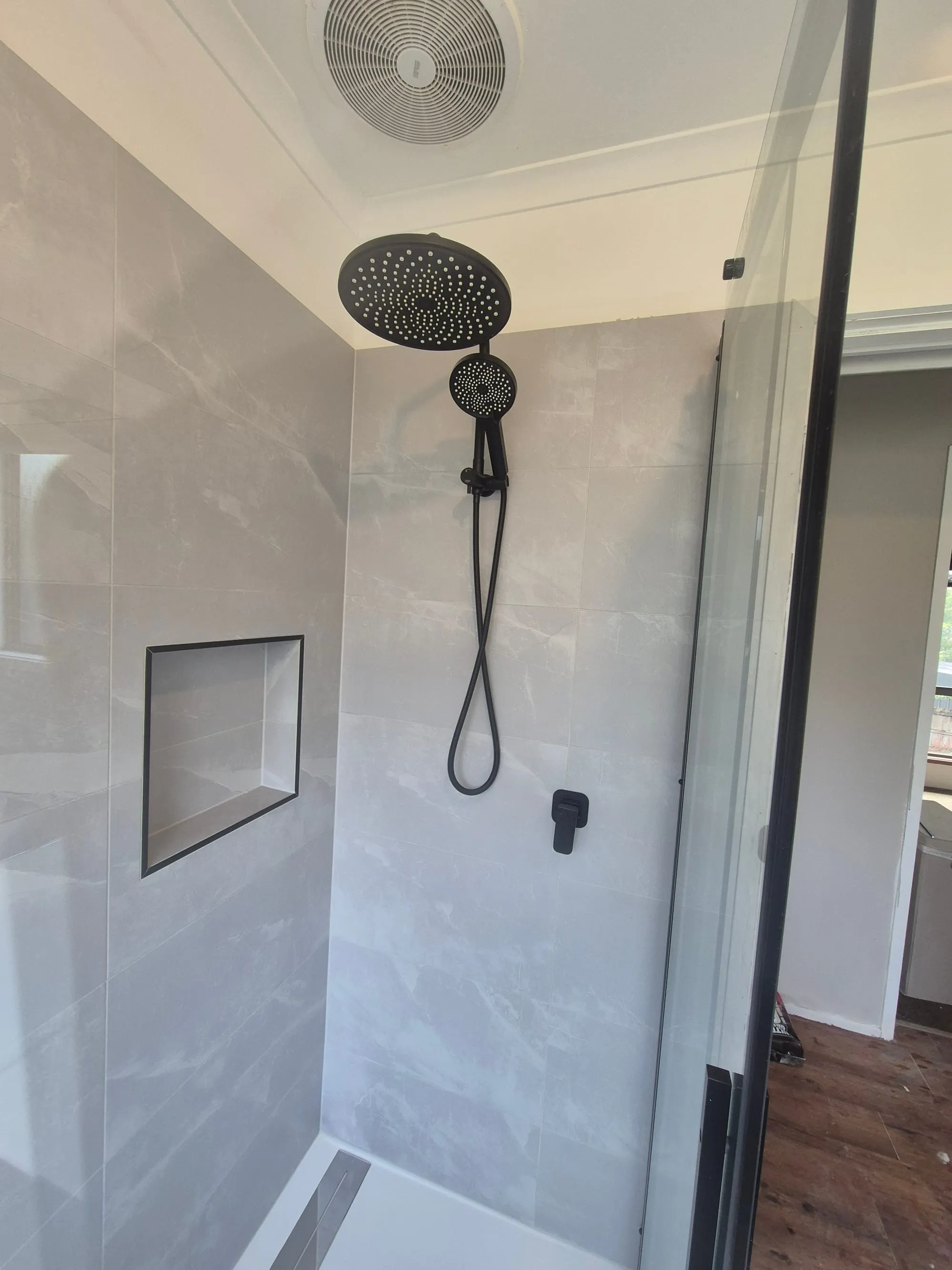 Black rain shower head and hand shower beside a recessed niche