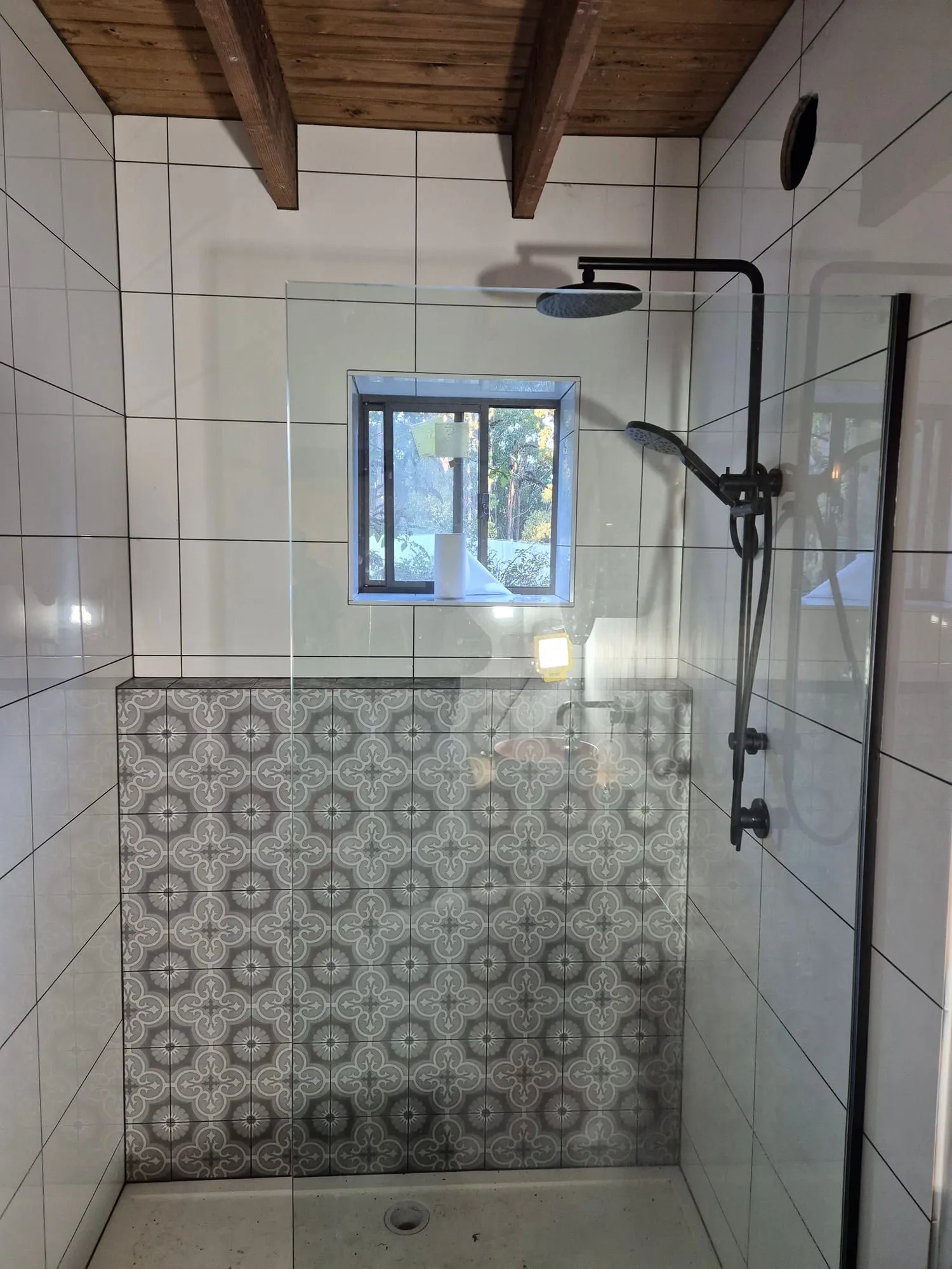 Shower with black tapware, a patterned tile floor and wall, and timber shelves alongside