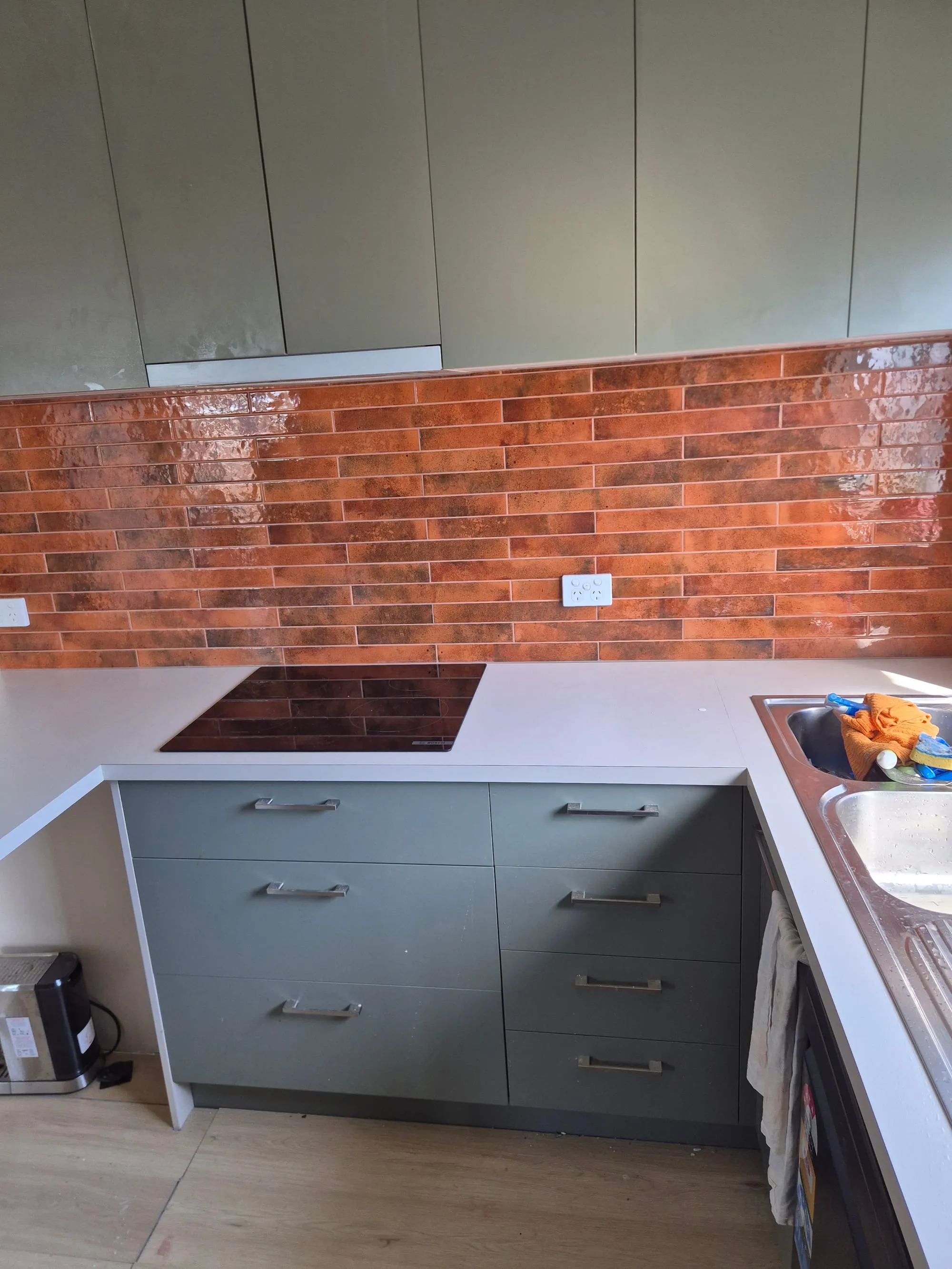 Kitchen with a red brick splashback, white benchtop and dark green cabinetry