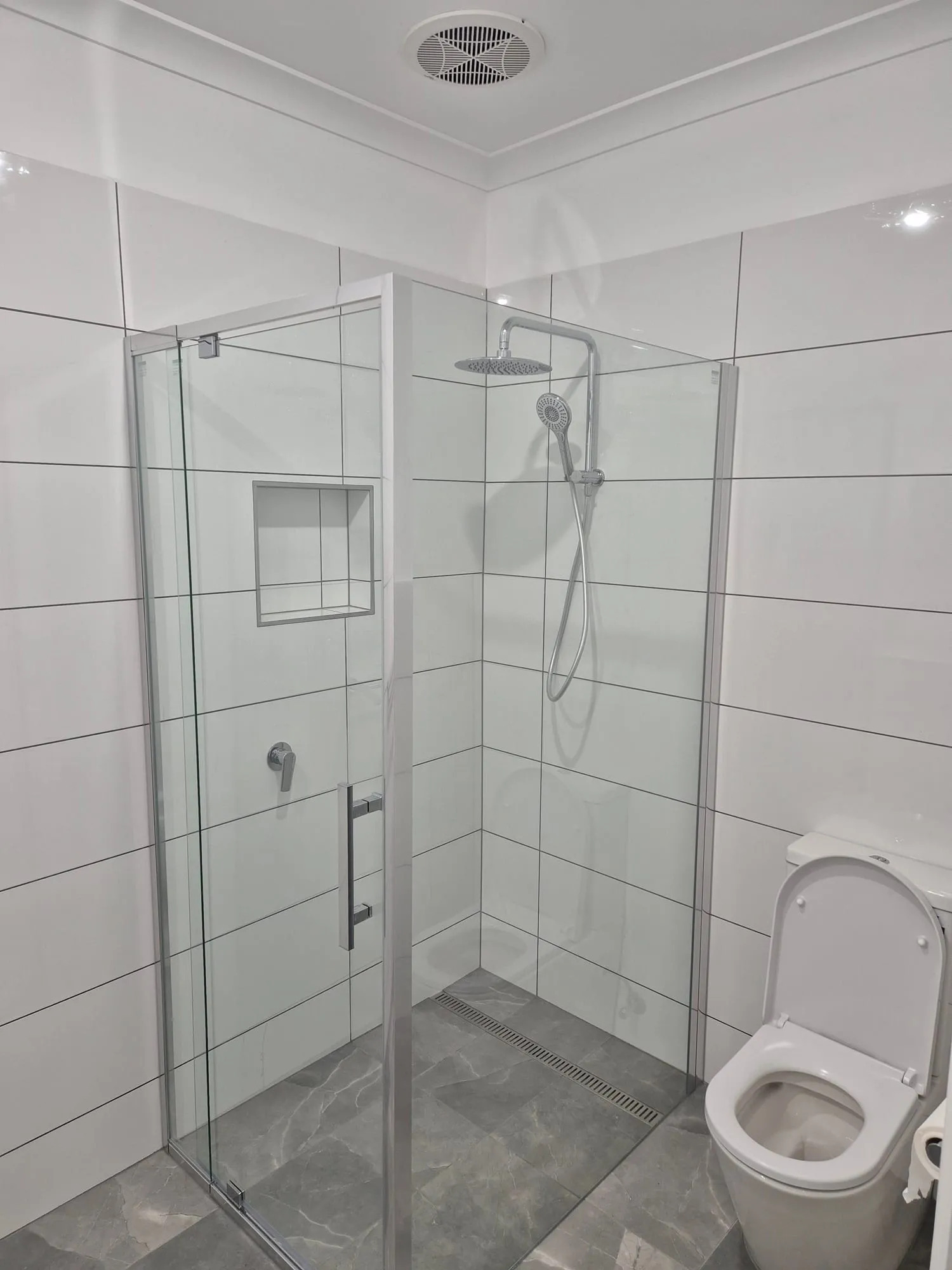 Frameless shower screen and toilet, in white wall tile with a grey stone-look floor