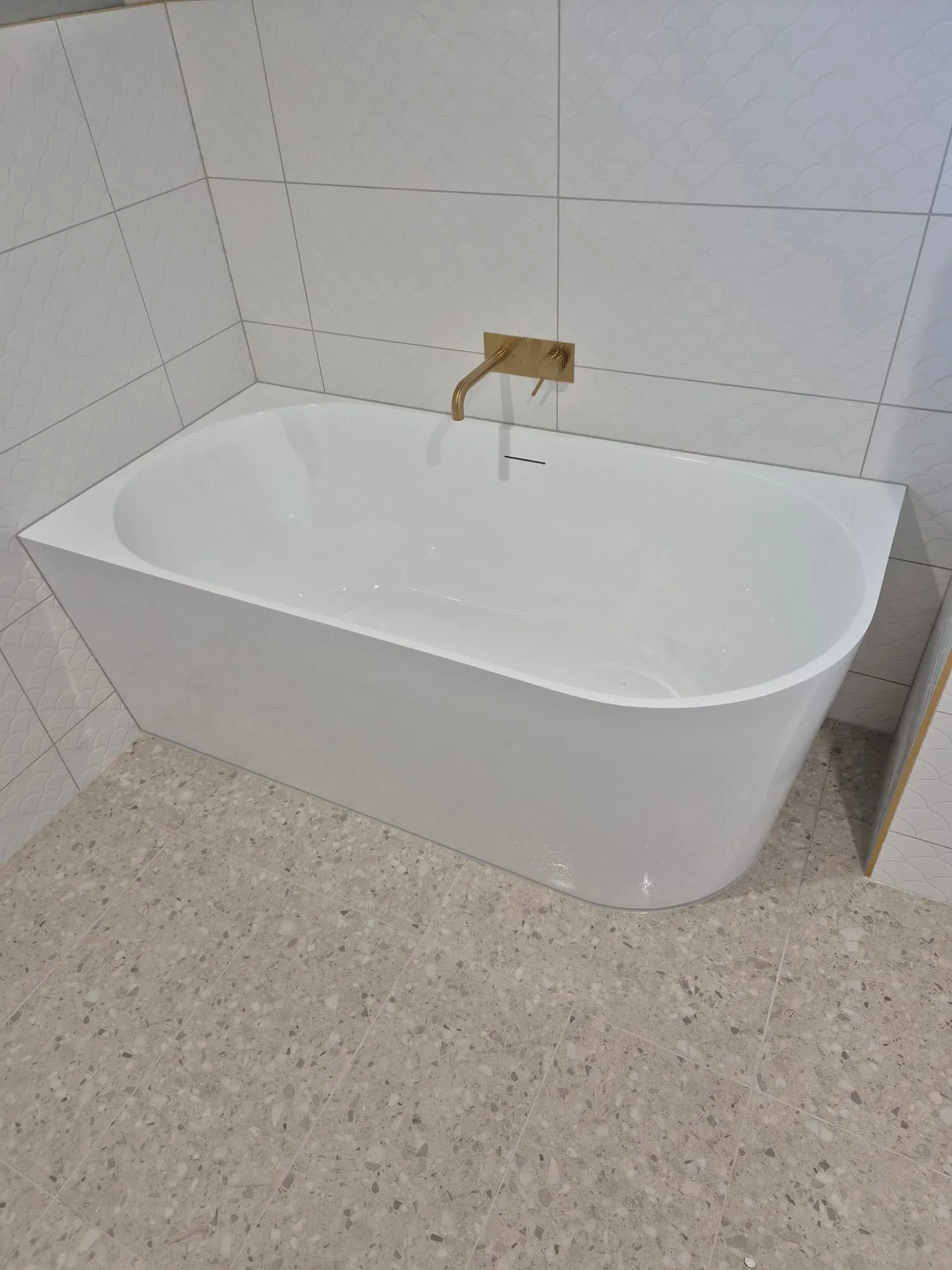 Freestanding bath with a wall-mounted brass spout, against scalloped white wall tile