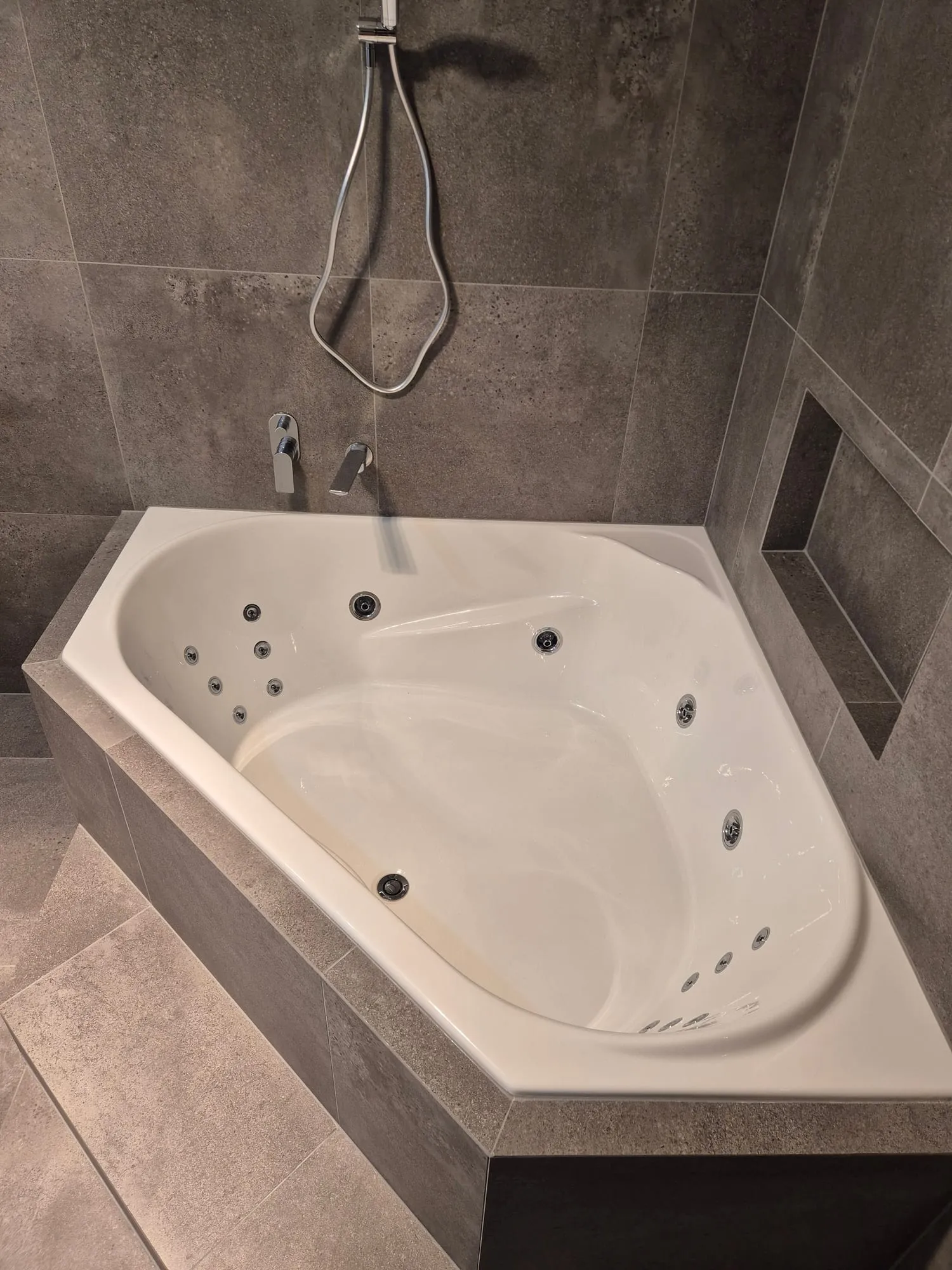 Corner spa bath and the tiled surround, with a recessed shelf above