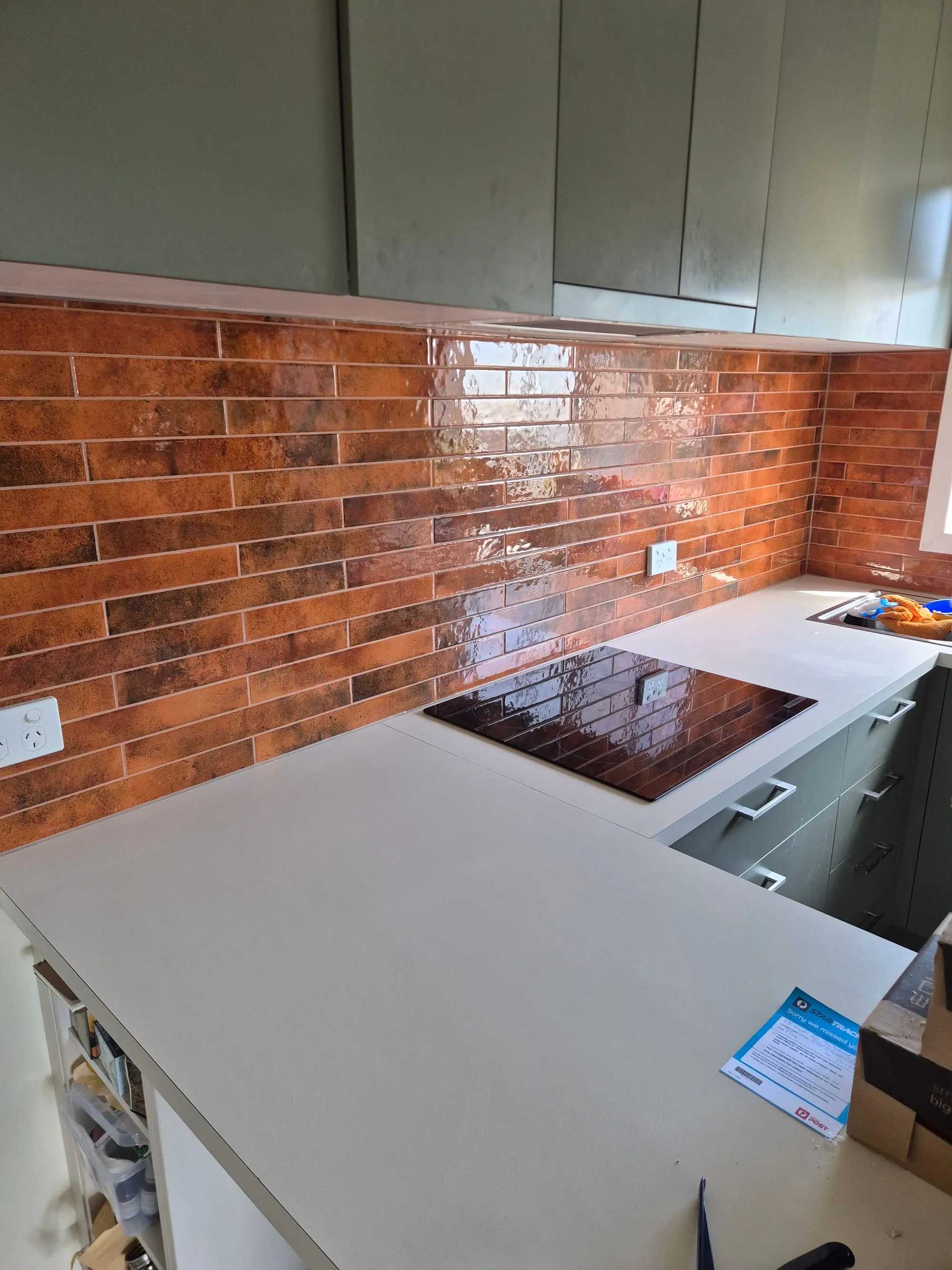 Red brick splashback behind a cooktop, with a white benchtop below