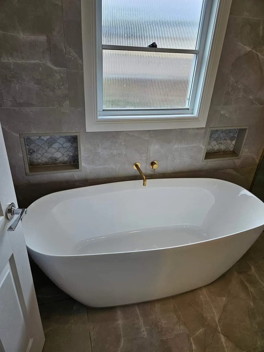 Freestanding bath below a window, between two fan-shaped mosaic niches