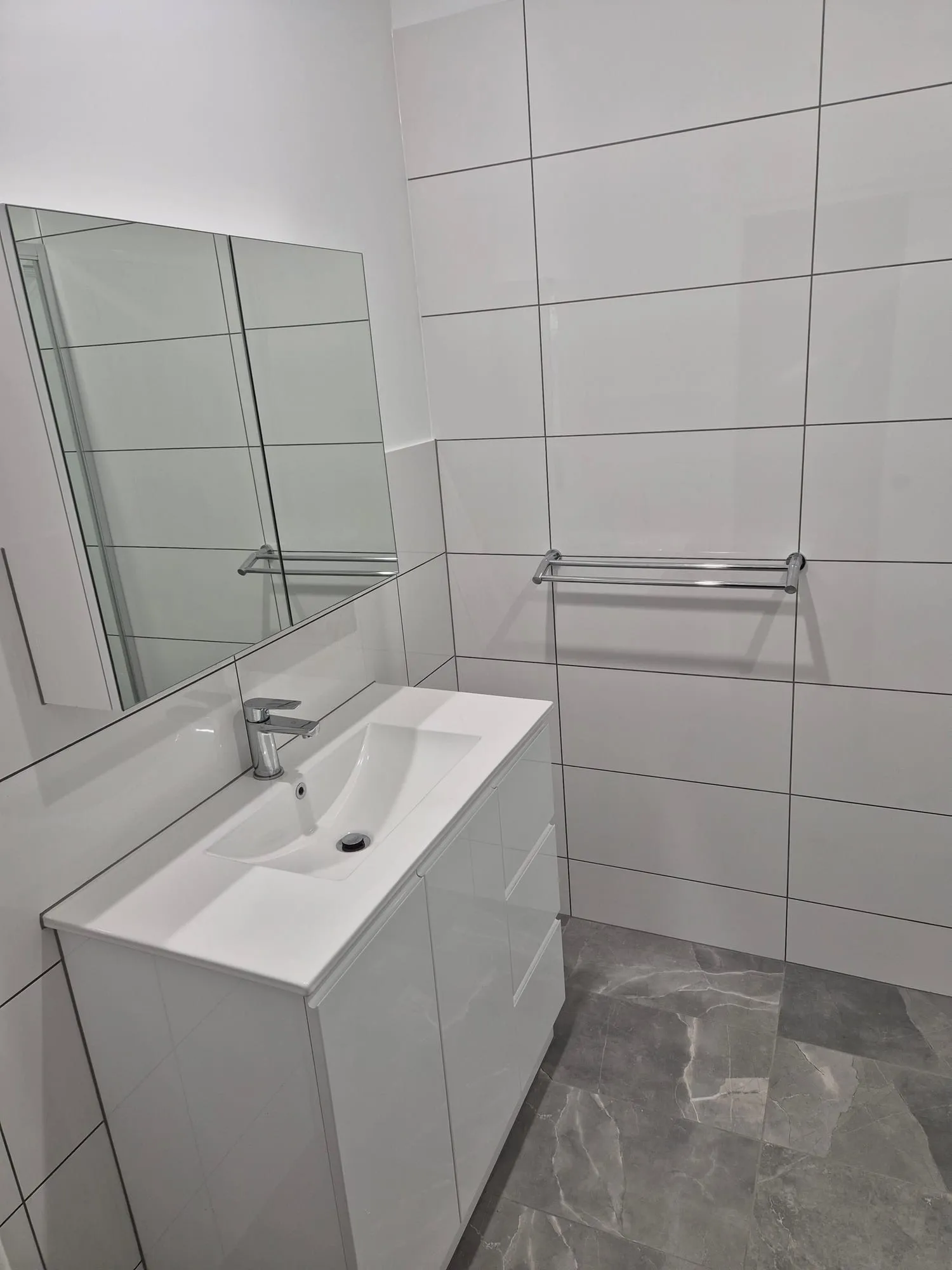 Wall-hung vanity below a mirror, with a towel rail on the tiled wall
