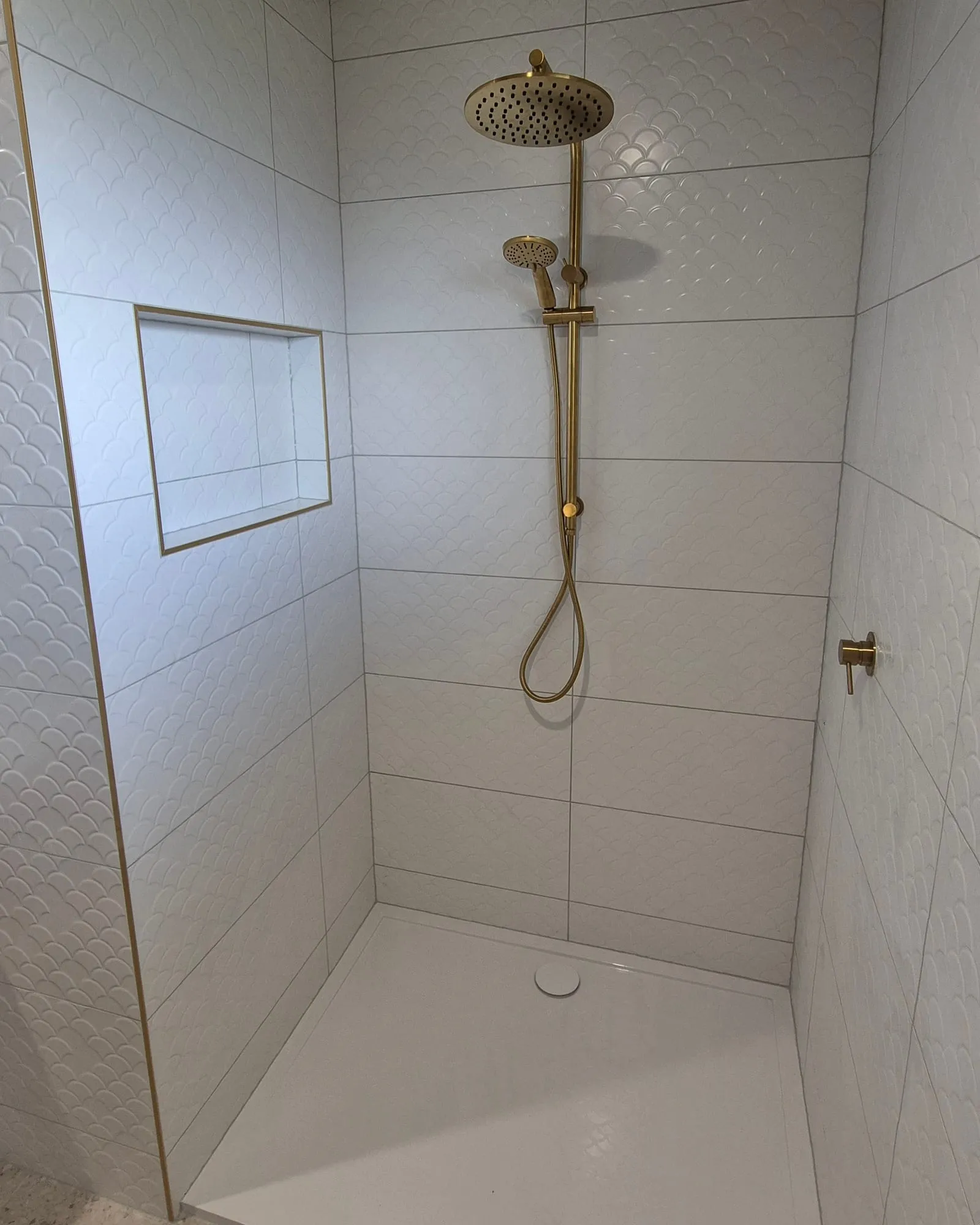 Shower with a brass rail shower and a recessed niche, in scalloped white tile