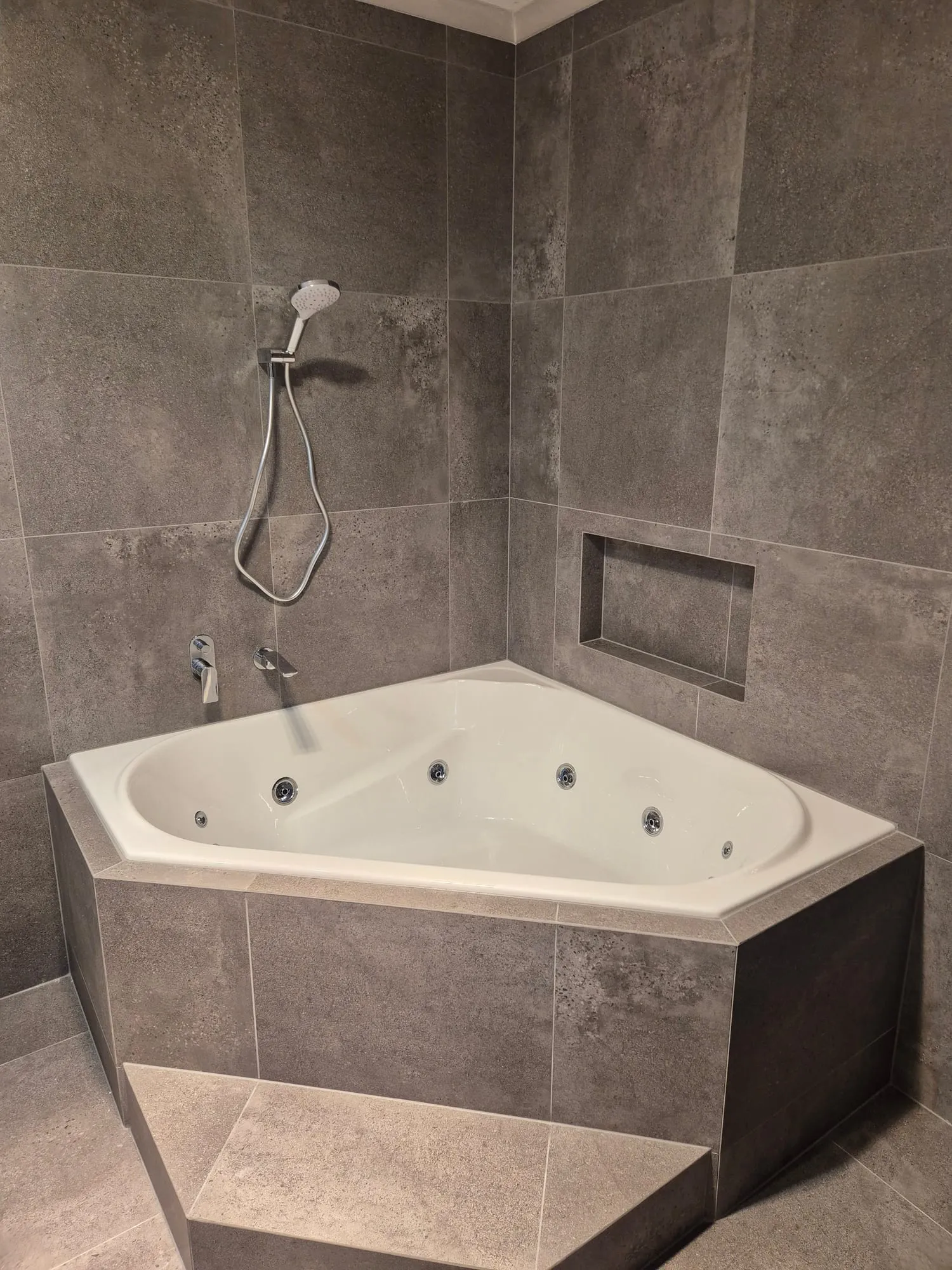 Corner spa bath with jets, set into large-format grey tile