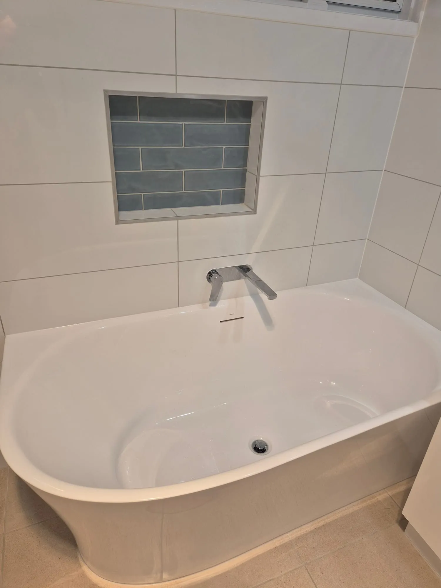 Corner bath with a wall-mounted mixer, below a blue subway tiled niche