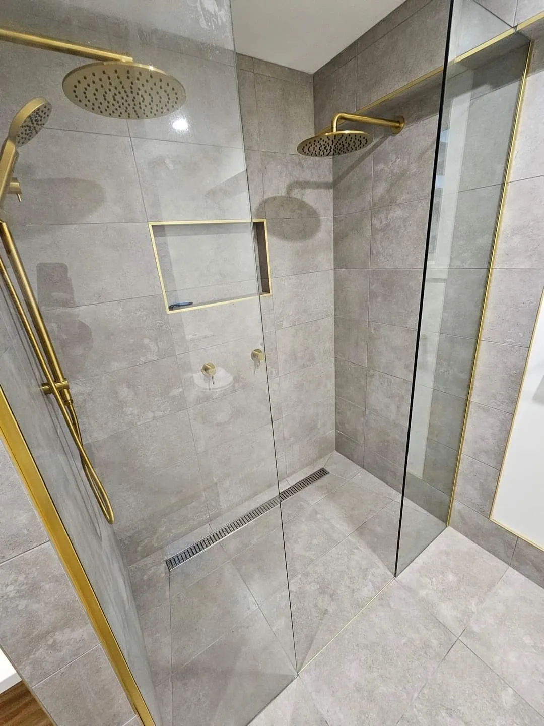 Double shower with brass shower heads, a brass-trimmed niche and a linear floor waste