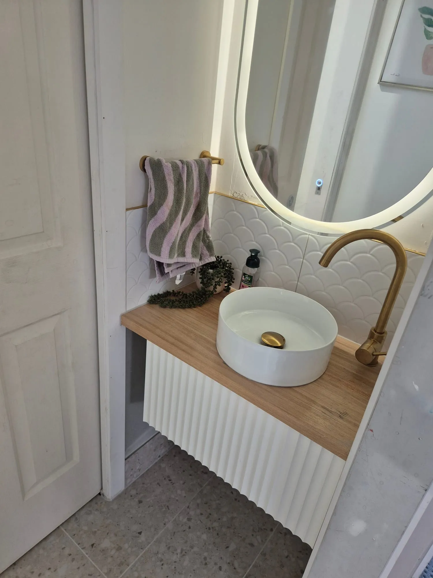 Round vessel basin on a timber top with a brass tap, below a backlit round mirror