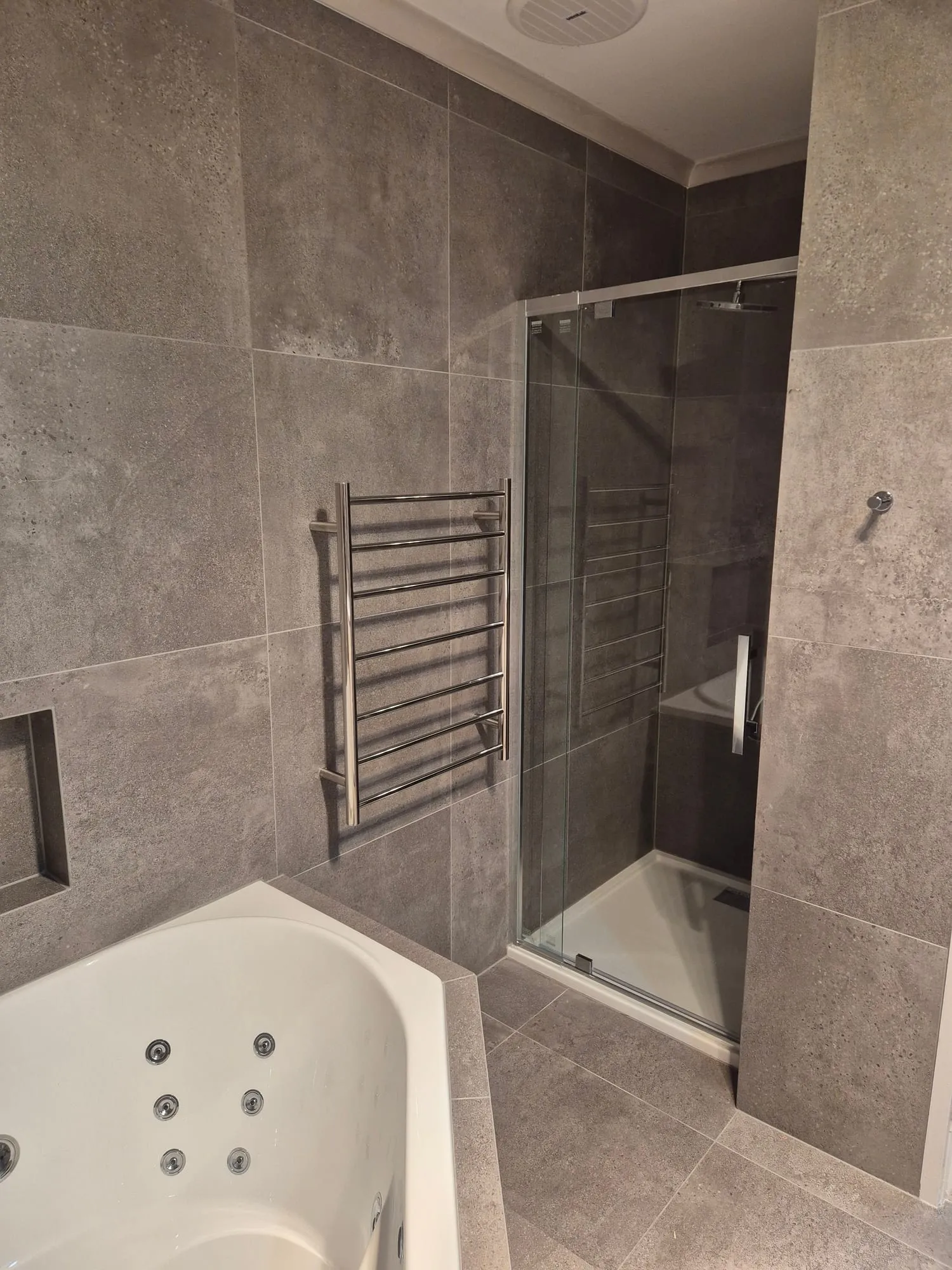 Shower with a glass screen and a heated towel rail beside the bath