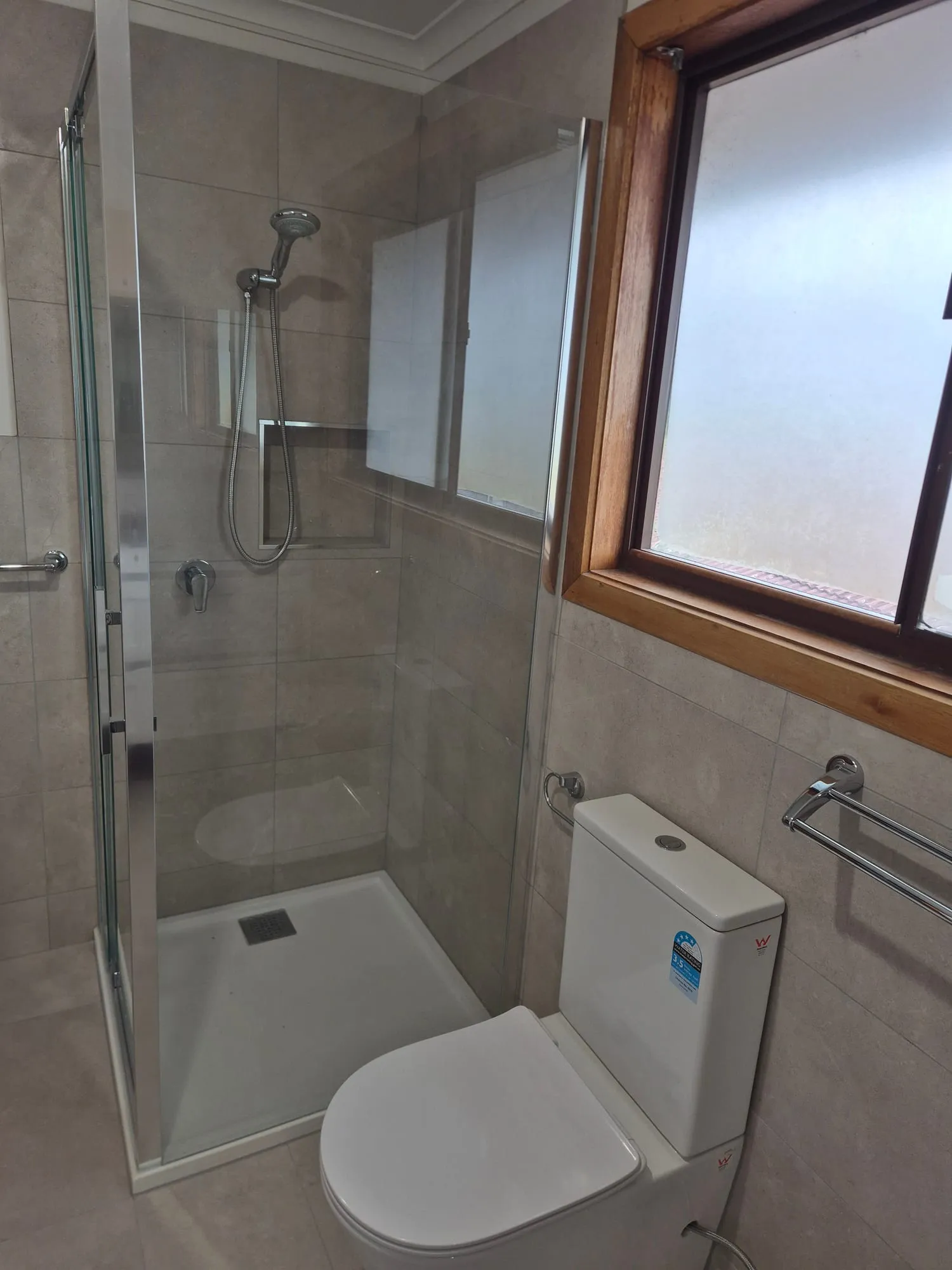 Shower with a glass door, beside the toilet and a timber-framed window